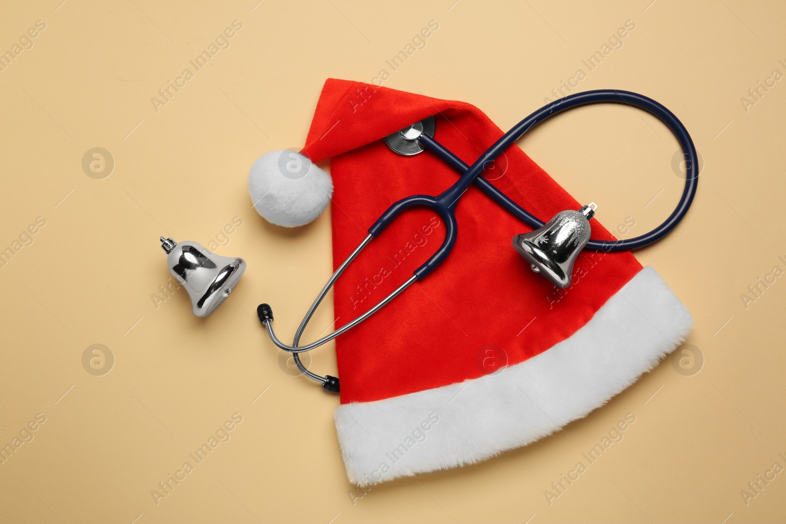 Photo of Greeting card for doctor with stethoscope, Santa hat and Christmas decor on beige background, flat lay