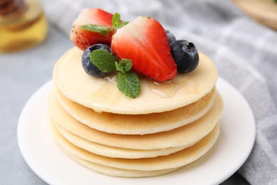 Stack of tasty pancakes with fresh berries, mint and honey on light grey table, closeup