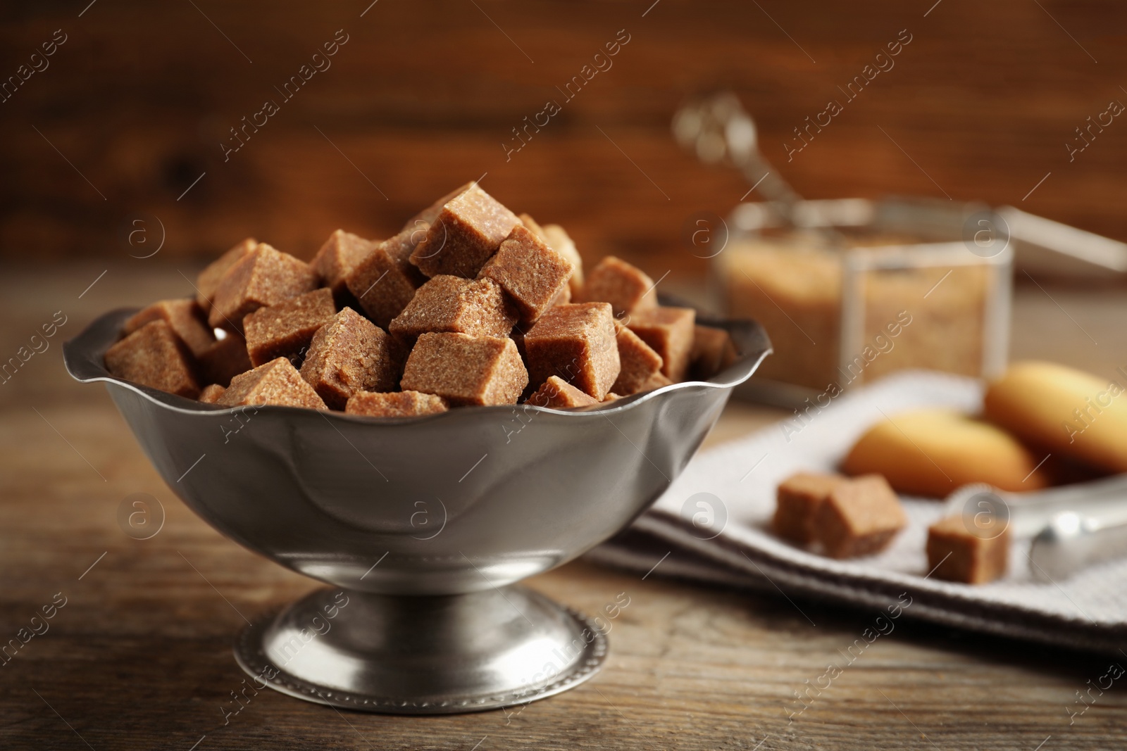 Photo of Brown sugar cubes in metal bowl on wooden table