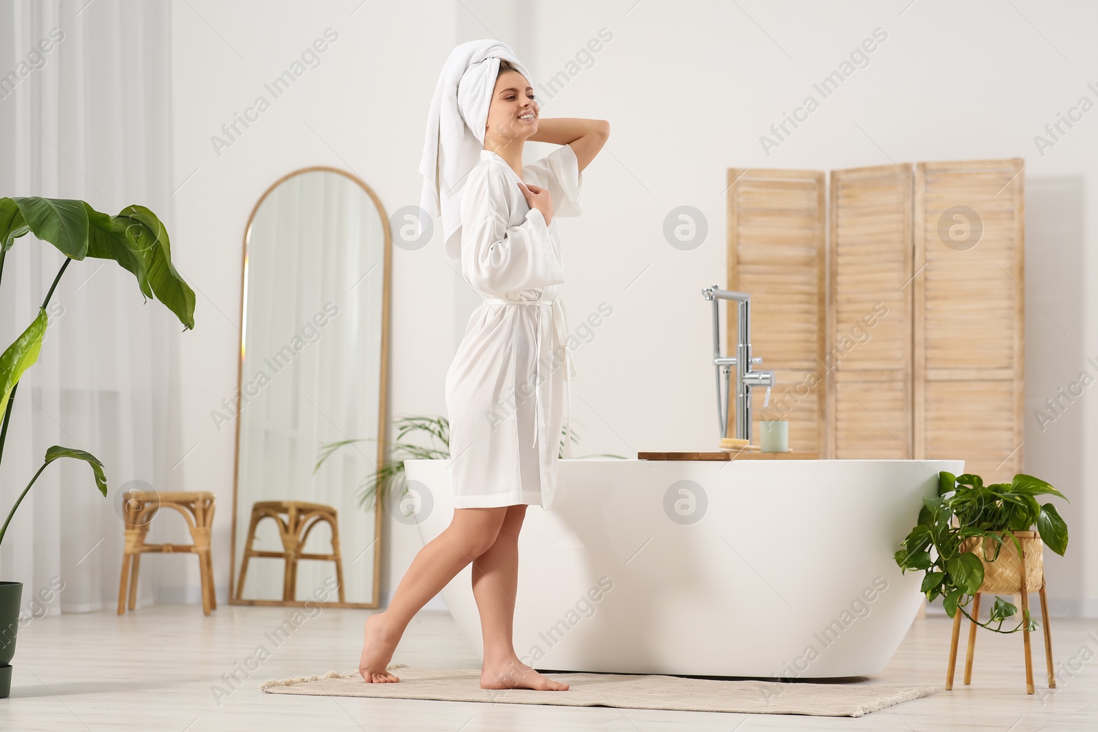 Photo of Beautiful happy woman wearing white robe near tub in bathroom