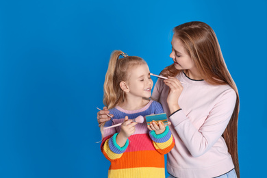 Photo of Happy mother applying powder onto daughter's face on blue background. Space for text