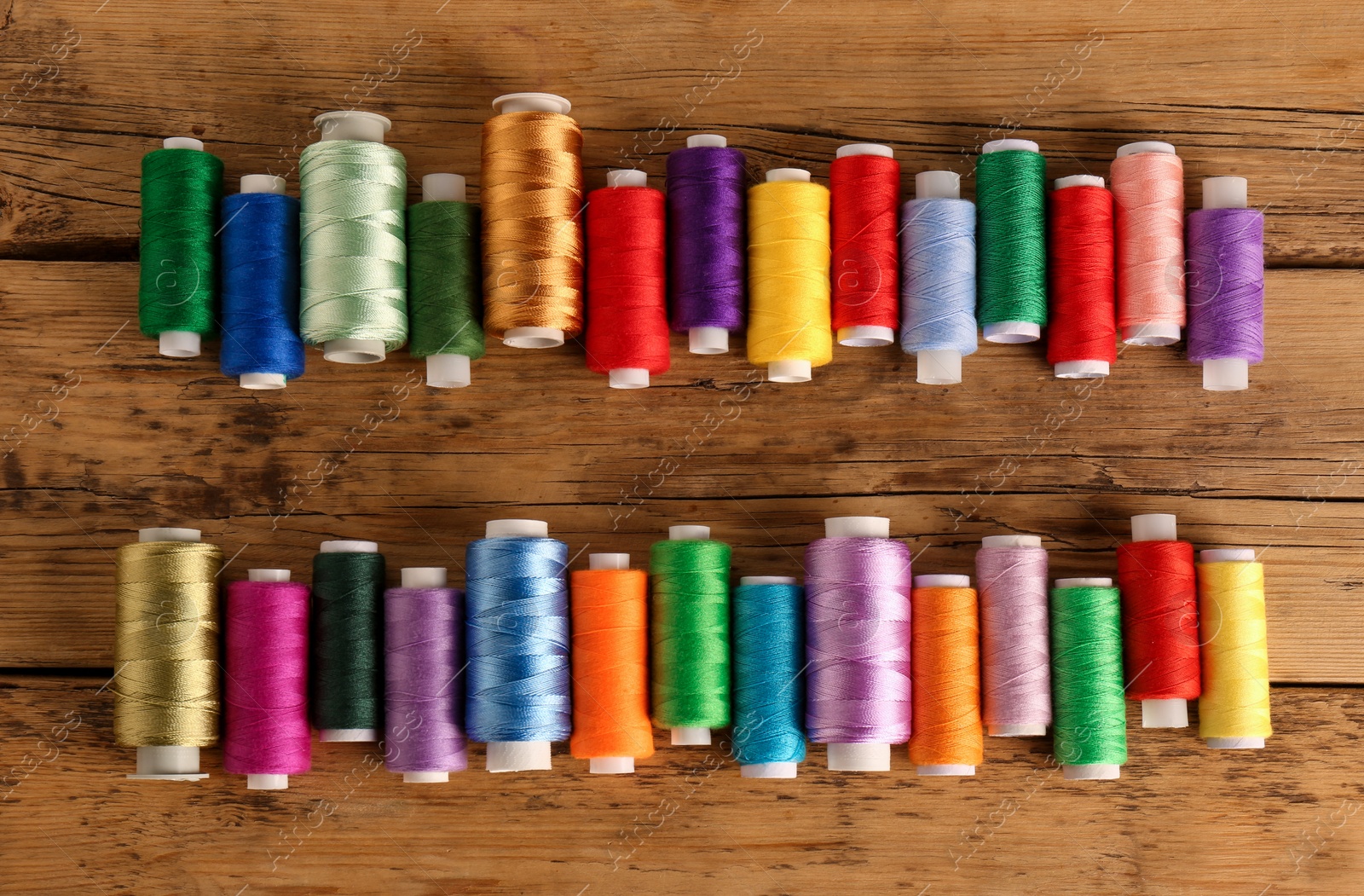 Photo of Different colorful sewing threads on wooden background, flat lay