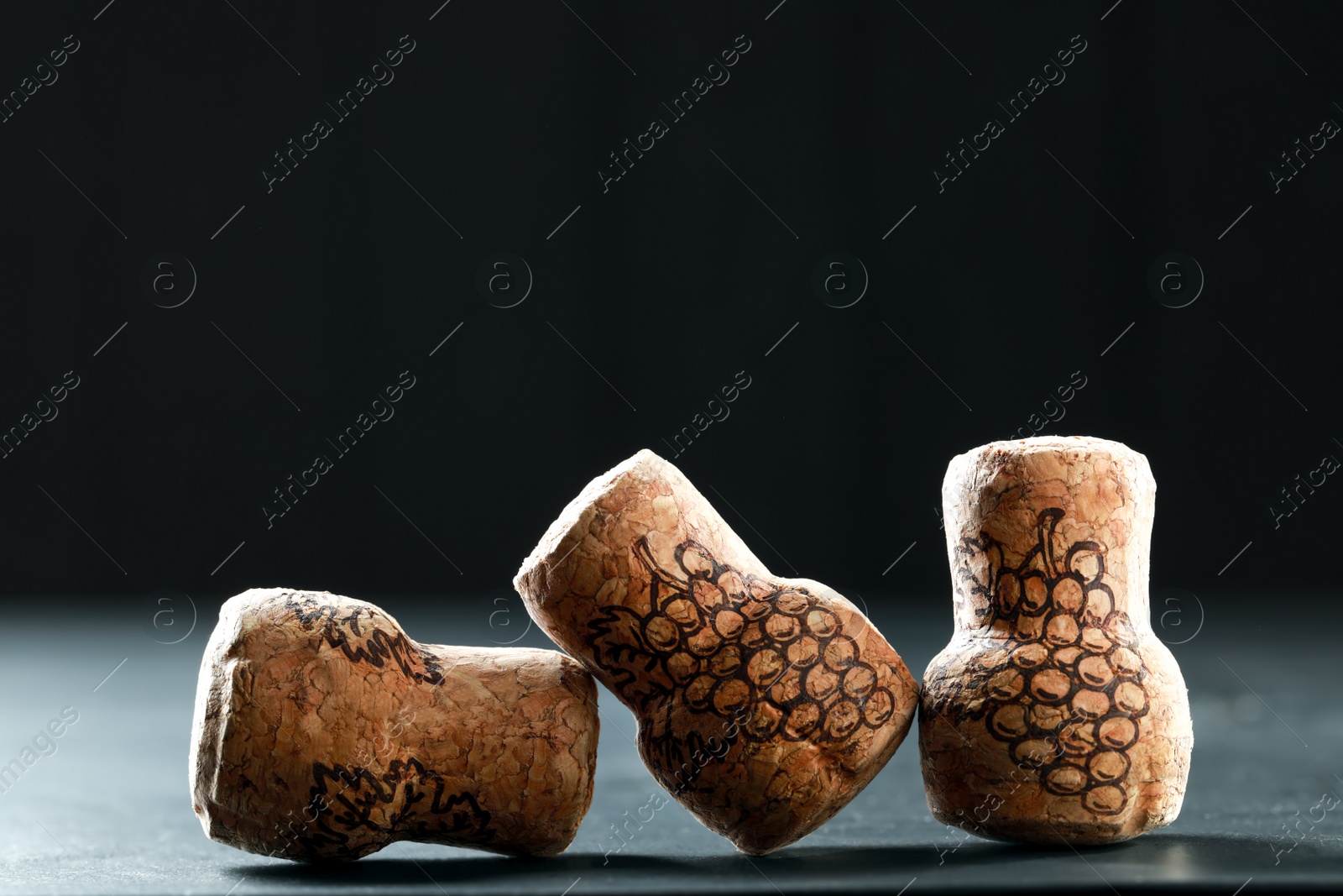 Photo of Corks of wine bottles with grape images on black table, closeup