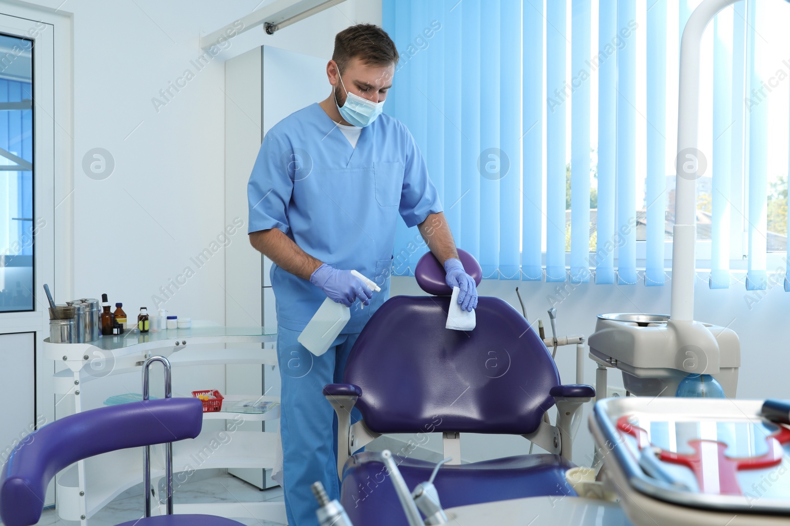 Photo of Professional dentist in uniform cleaning workplace  with antiseptic indoors