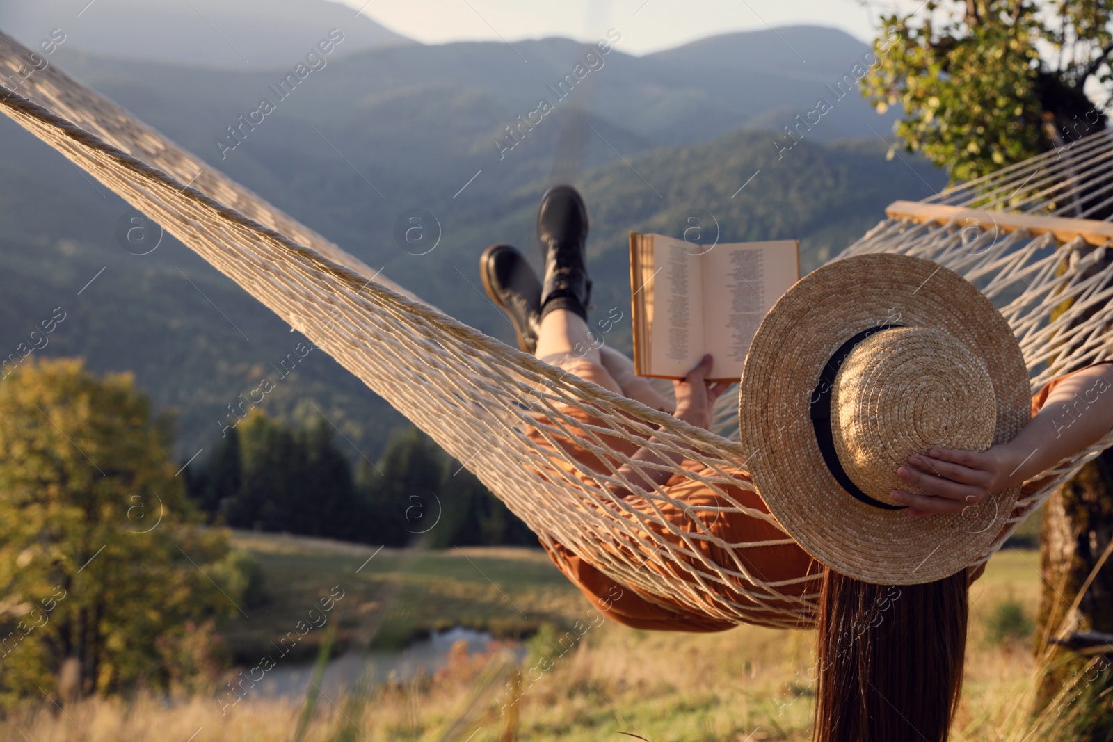 Photo of Young woman reading book in hammock outdoors at sunset