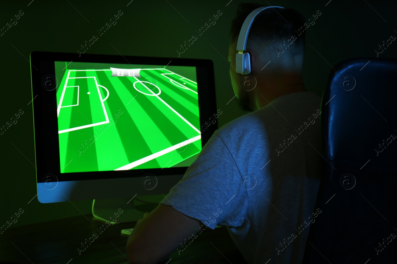 Photo of Man with headphones playing video game on modern computer in dark room