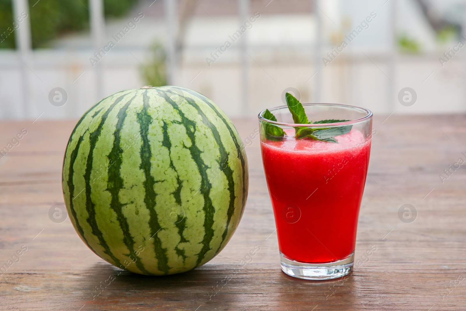 Photo of Glass of delicious watermelon smoothie with mint and fresh fruit on wooden table outdoors