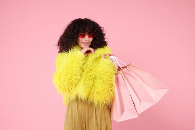 Happy young woman with shopping bags on pink background