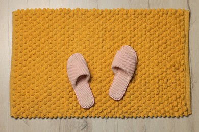 Photo of Soft orange bath mat and slippers on floor, top view