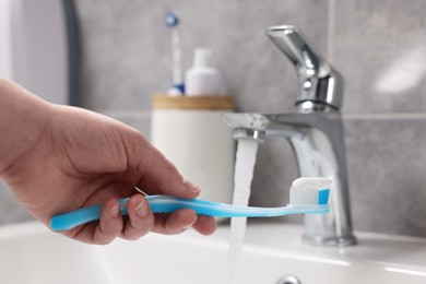 Photo of Woman holding plastic toothbrush with paste near flowing water above sink in bathroom, closeup