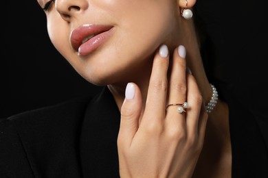 Young woman with elegant pearl jewelry on black background, closeup