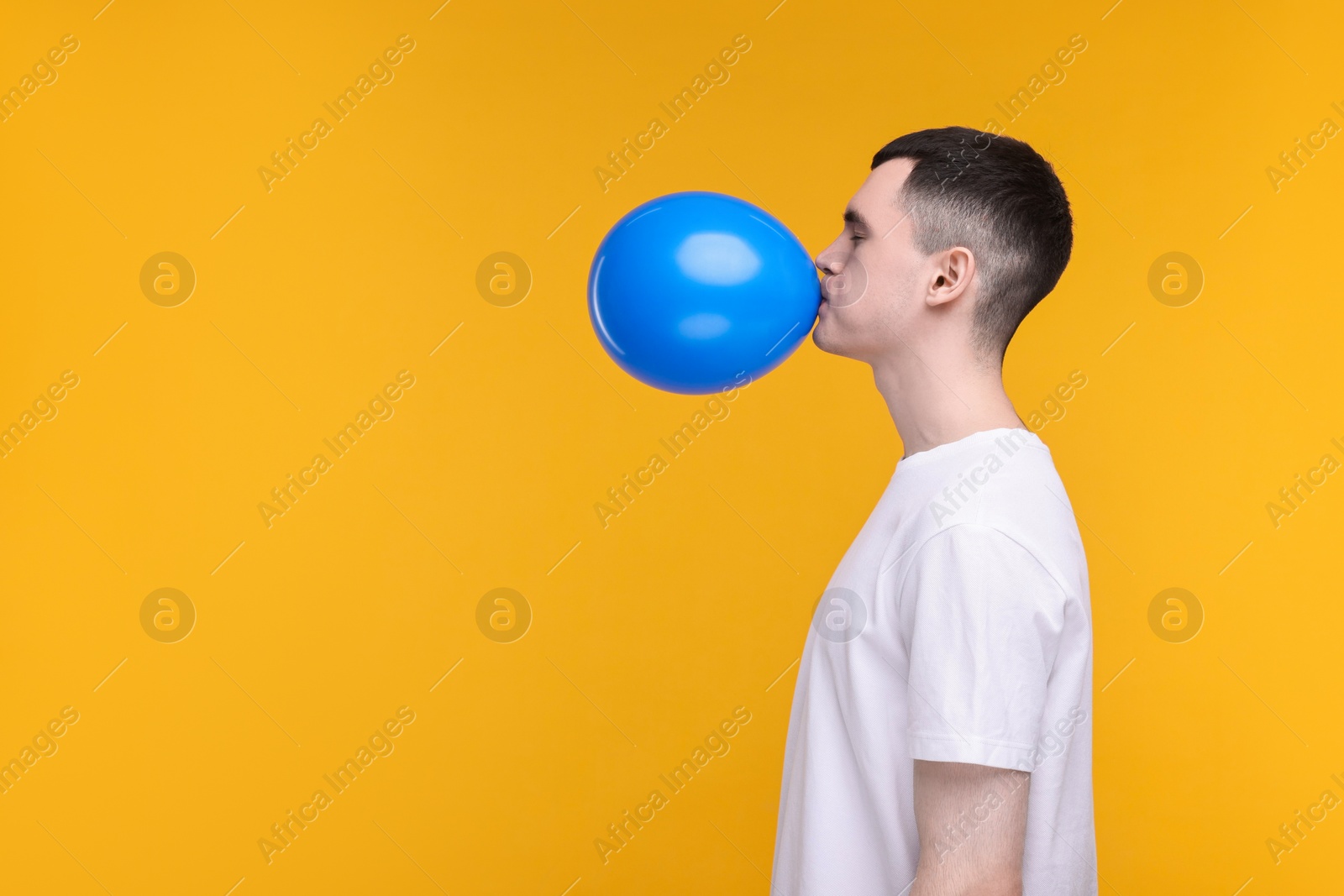 Photo of Young man inflating light blue balloon on yellow background. Space for text