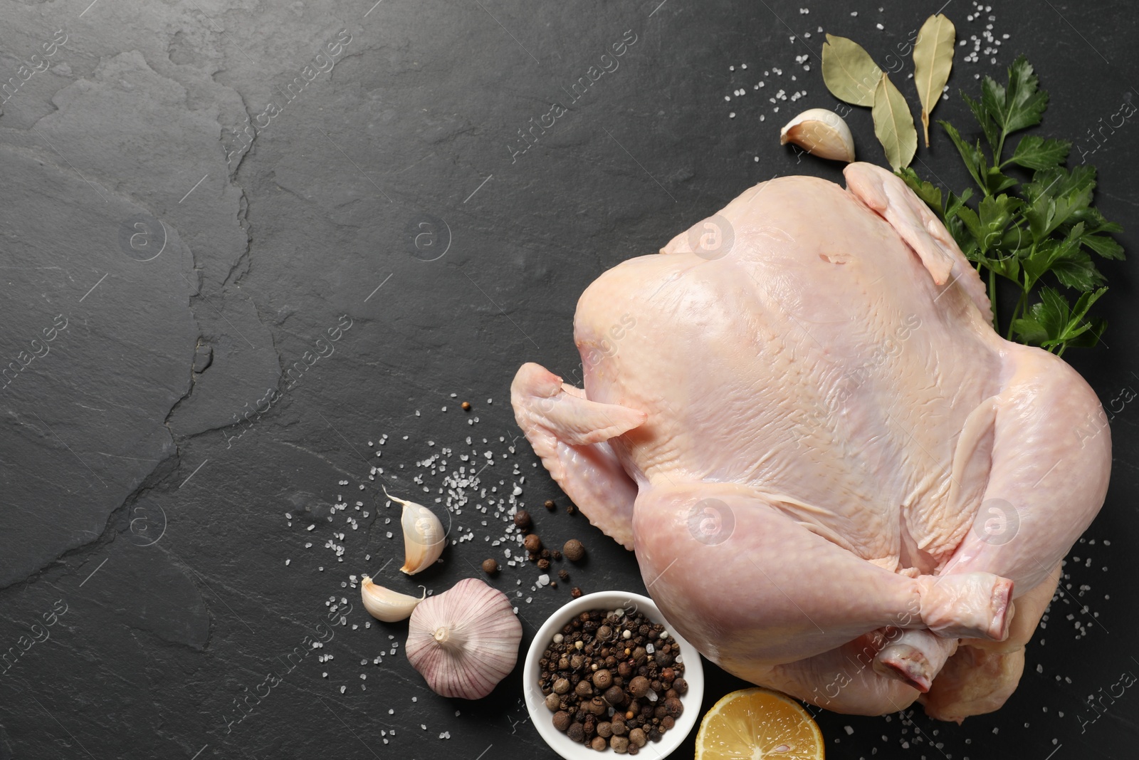 Photo of Fresh raw chicken with spices and lemon on black textured table, flat lay. Space for text