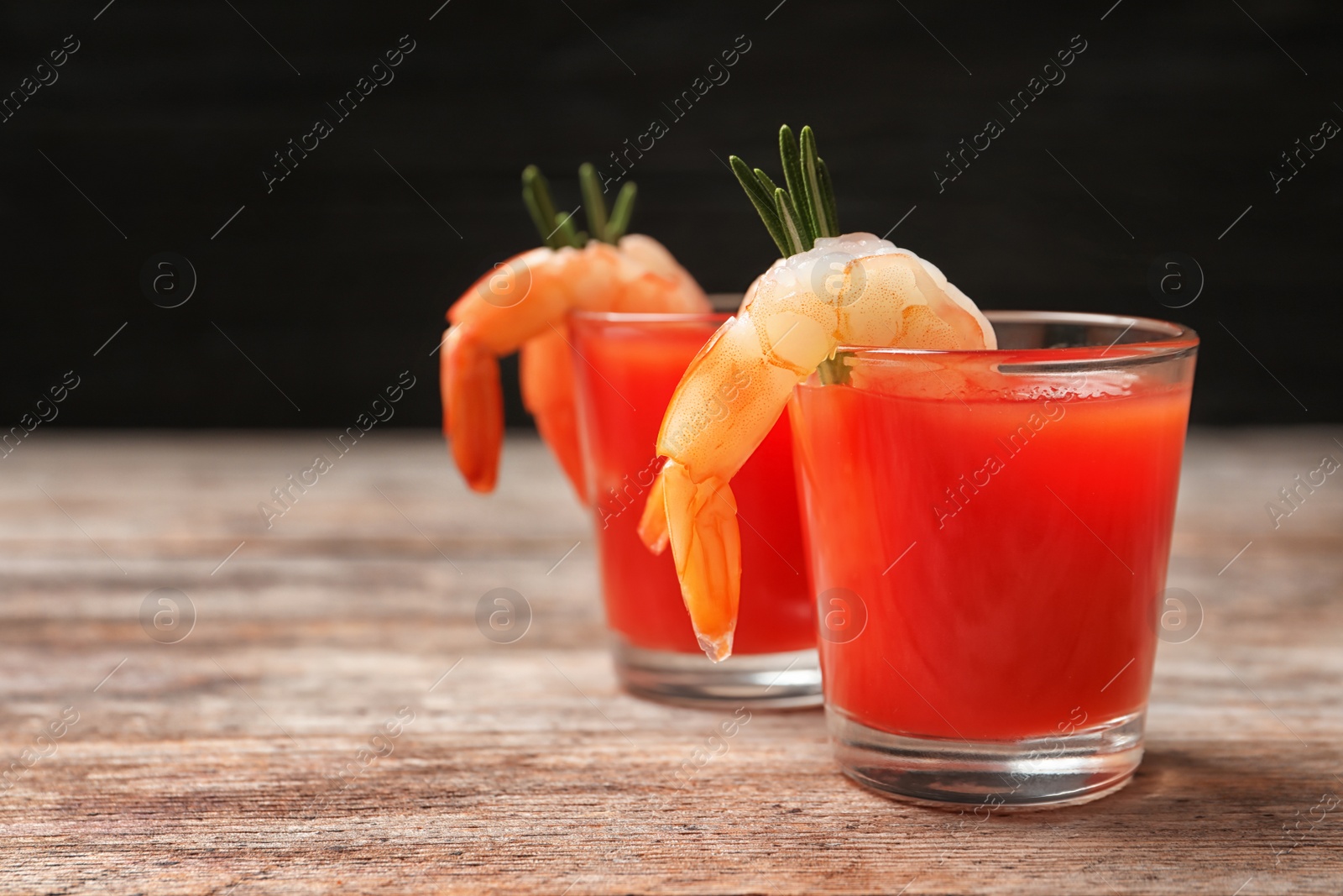 Photo of Delicious shrimp cocktail shots on wooden table against dark background