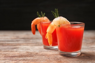 Photo of Delicious shrimp cocktail shots on wooden table against dark background