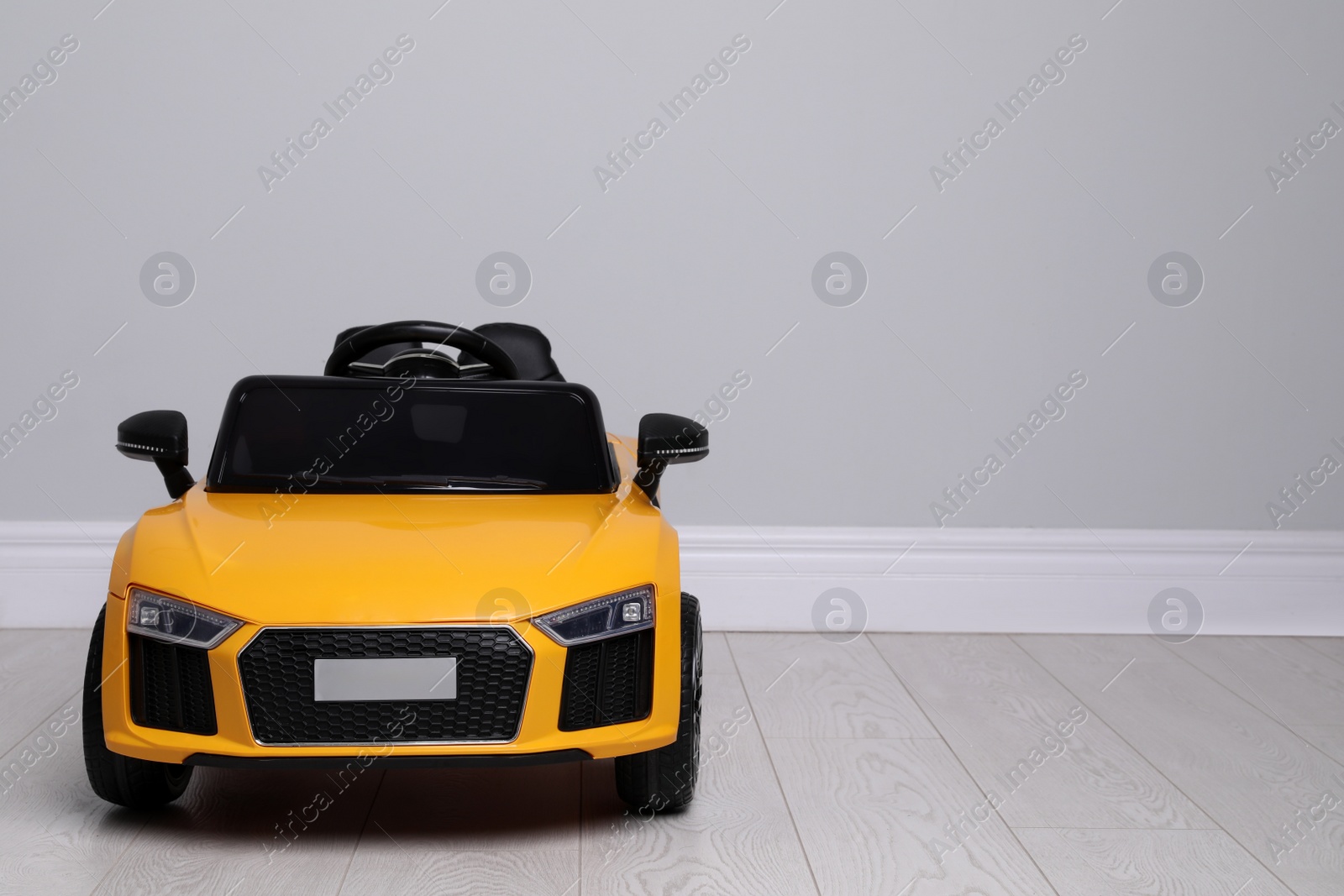 Photo of Child's electric toy car near light wall indoors. Space for text