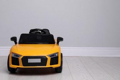 Child's electric toy car near light wall indoors. Space for text