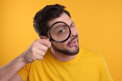 Photo of Curious man looking through magnifier glass on yellow background