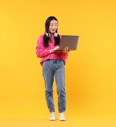 Portrait of smiling woman with headphones and laptop on orange background