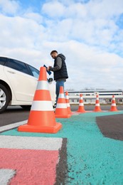 Photo of Instructor with clipboard near car outdoors, focus on traffic cone. Driving school exam