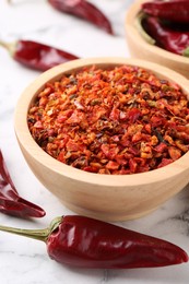 Chili pepper flakes in bowl and pods on white marble table, closeup