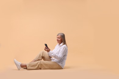 Photo of Senior woman with phone on beige background, space for text