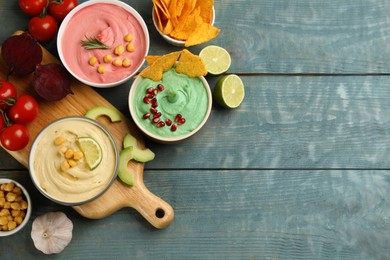 Photo of Different kinds of tasty hummus served with nachos on light blue wooden table, flat lay. Space for text