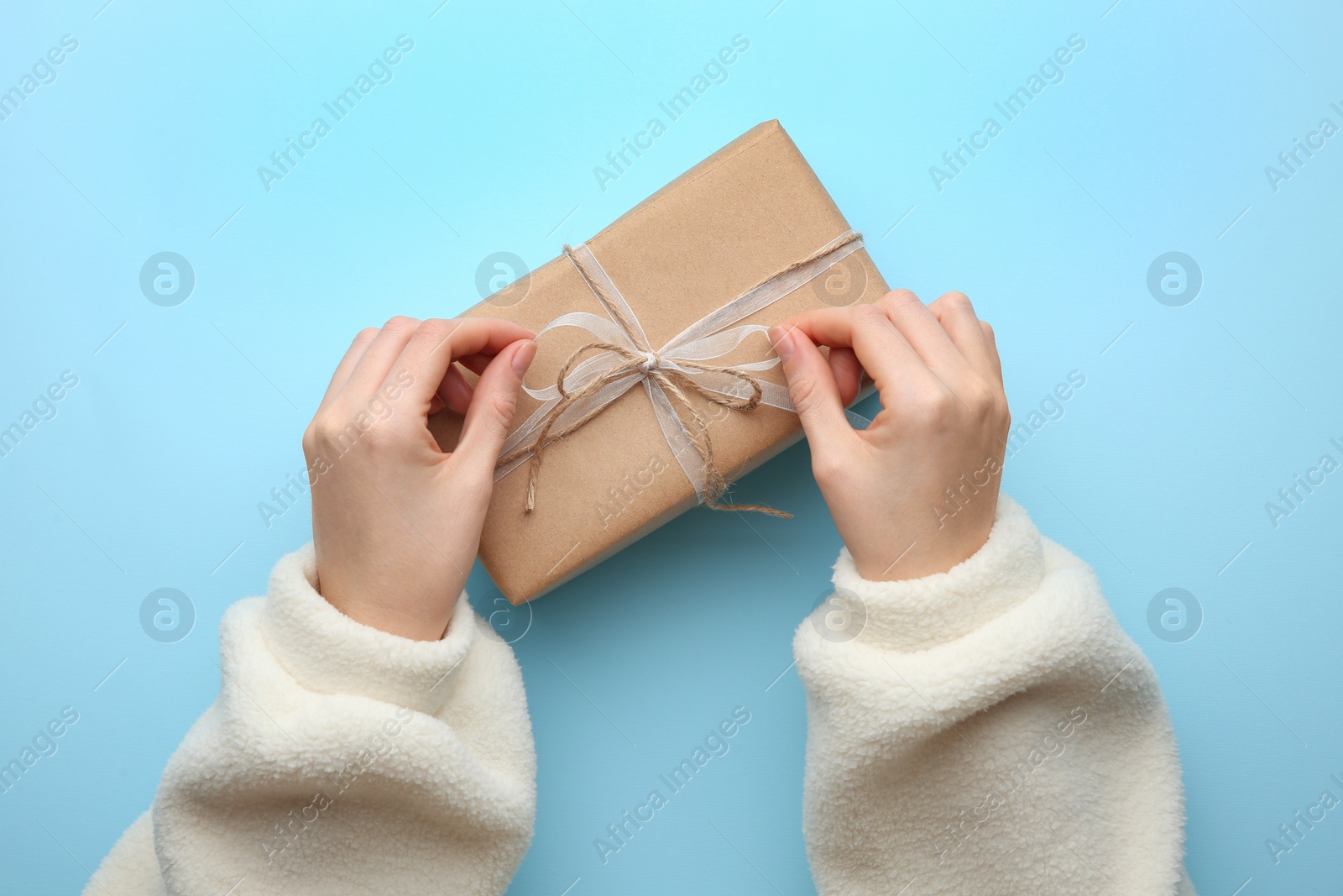 Photo of Woman holding Christmas gift box on light blue background, top view