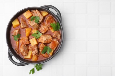 Photo of Delicious goulash in pot on white tiled table, top view. Space for text