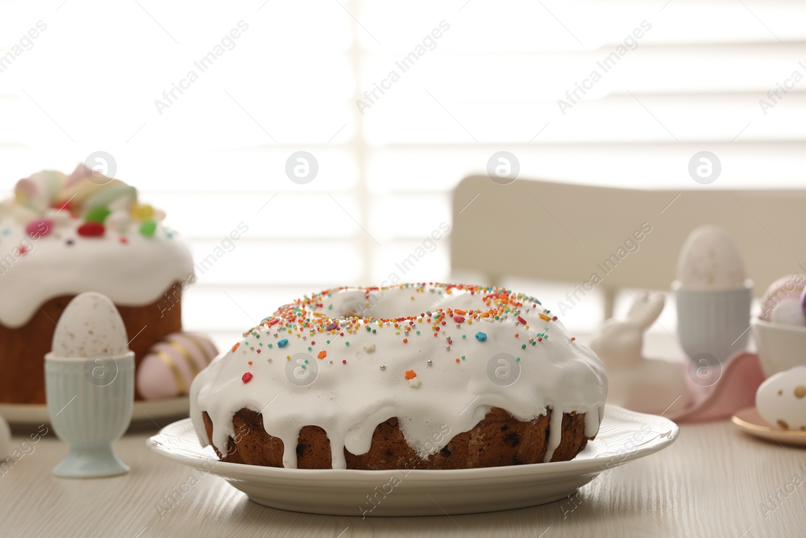 Photo of Delicious Easter cake decorated with sprinkles near painted eggs on white wooden table