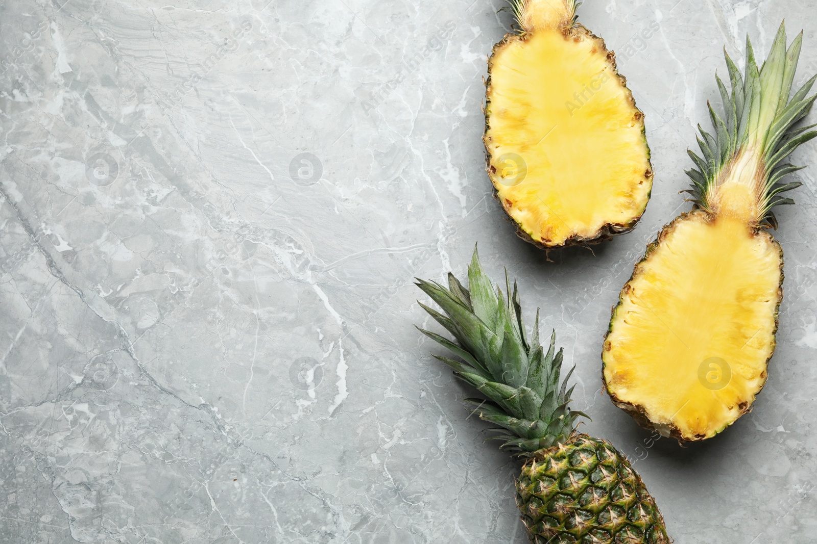 Photo of Fresh whole and cut pineapples on gray marble background, top view. Space for text