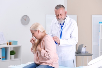 Doctor examining coughing mature woman at clinic