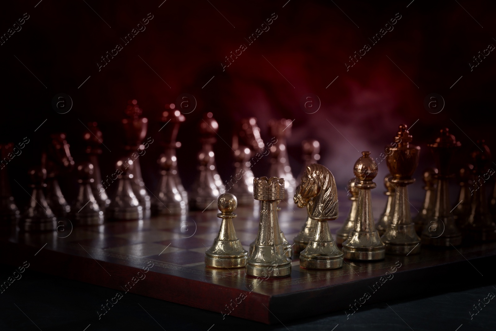 Image of Chessboard with game pieces in starting position surrounded by smoke on black background