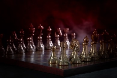 Chessboard with game pieces in starting position surrounded by smoke on black background