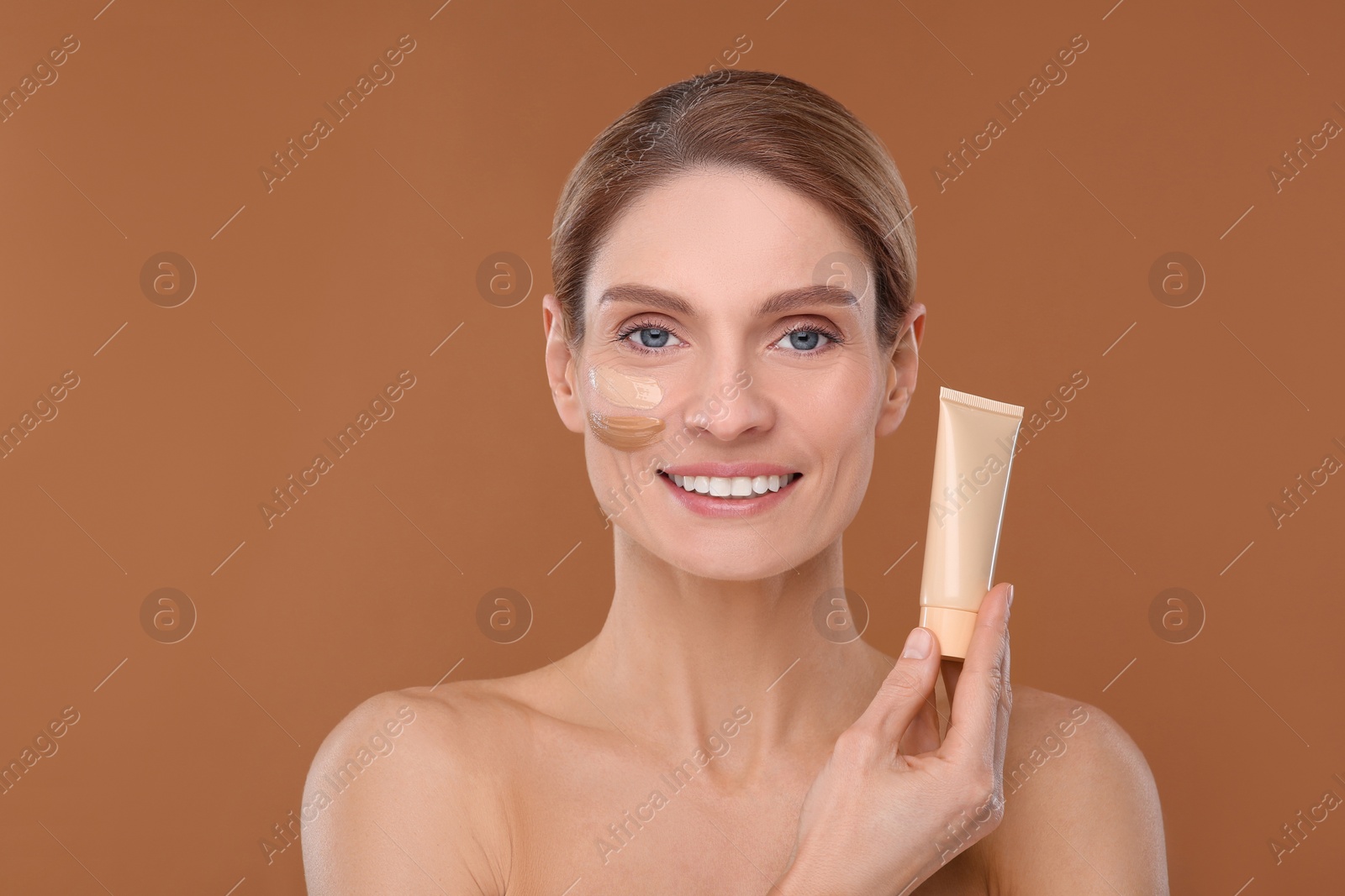 Photo of Woman holding tube of foundation on brown background. Space for text