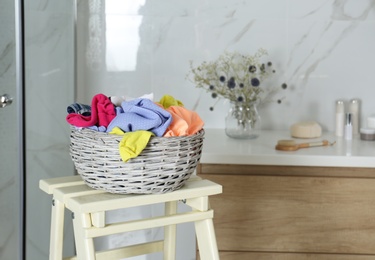 Wicker laundry basket with different clothes on wooden stool in bathroom. Space for text