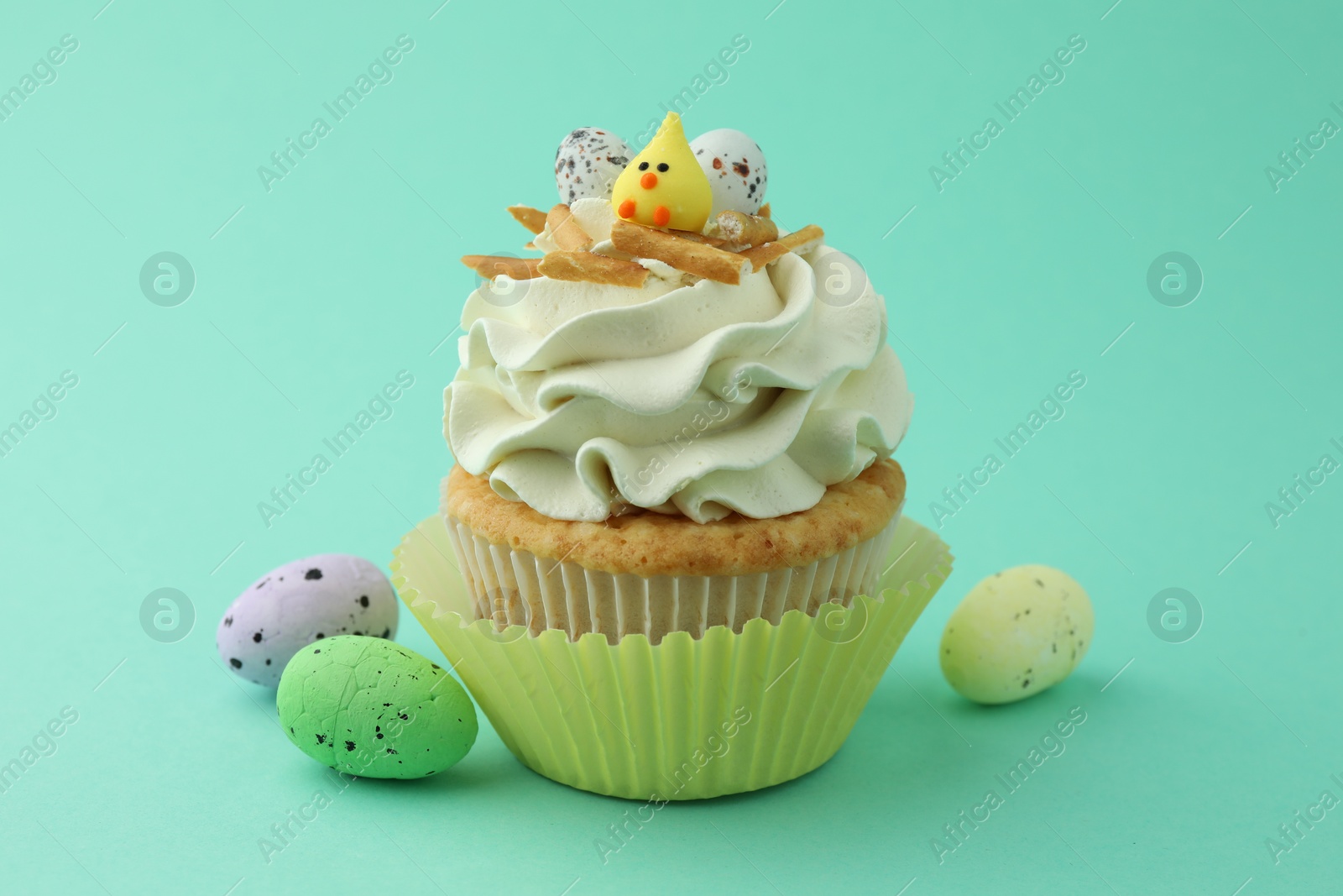 Photo of Tasty Easter cupcake with vanilla cream and candies on turquoise background