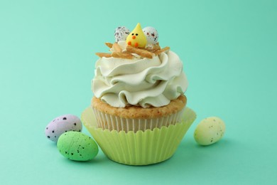 Photo of Tasty Easter cupcake with vanilla cream and candies on turquoise background