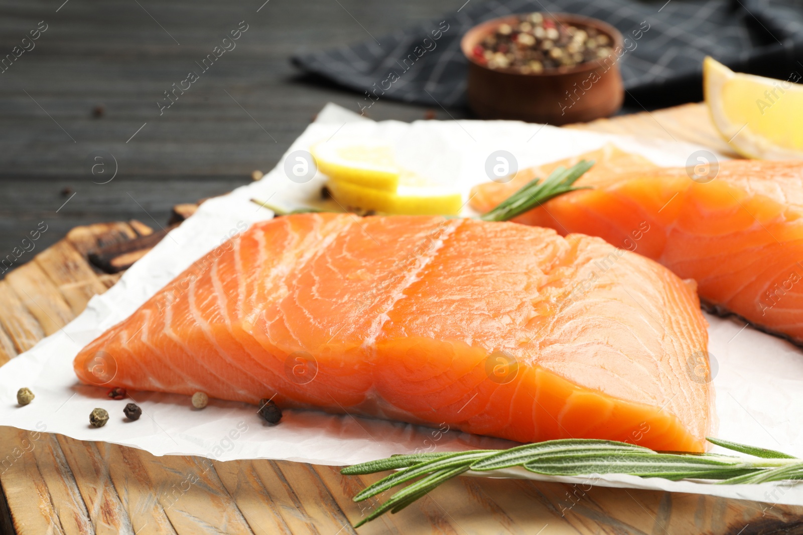 Photo of Wooden board with tasty salmon fillet on dark table, closeup