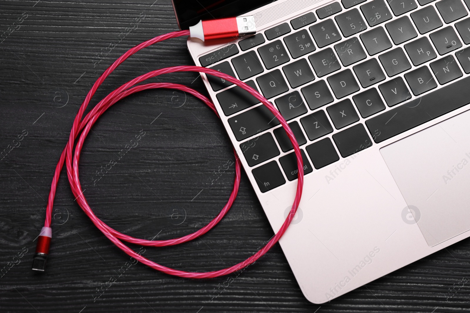 Photo of Red USB cable with type C connector and laptop on black wooden table, flat lay