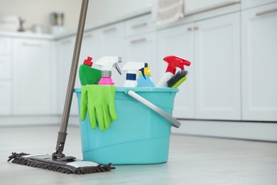 Photo of Mop and plastic bucket with different cleaning supplies in kitchen
