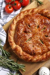 Photo of Tasty homemade pie, rosemary and tomatoes on wooden table, flat lay