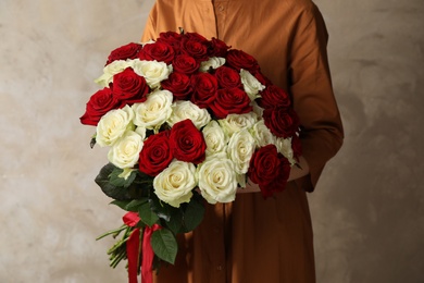 Photo of Woman holding luxury bouquet of fresh roses on beige background, closeup