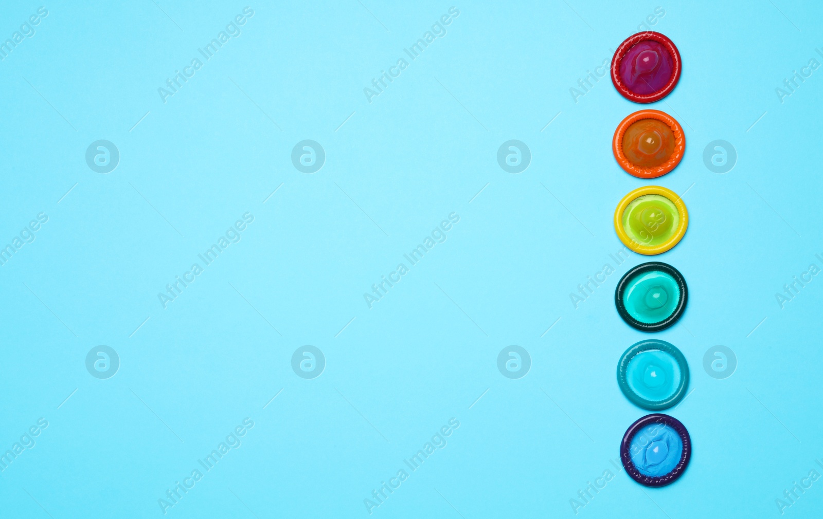 Photo of Colorful condoms on light blue background, flat lay. LGBT concept