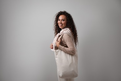 Happy African-American woman with eco bag on grey background