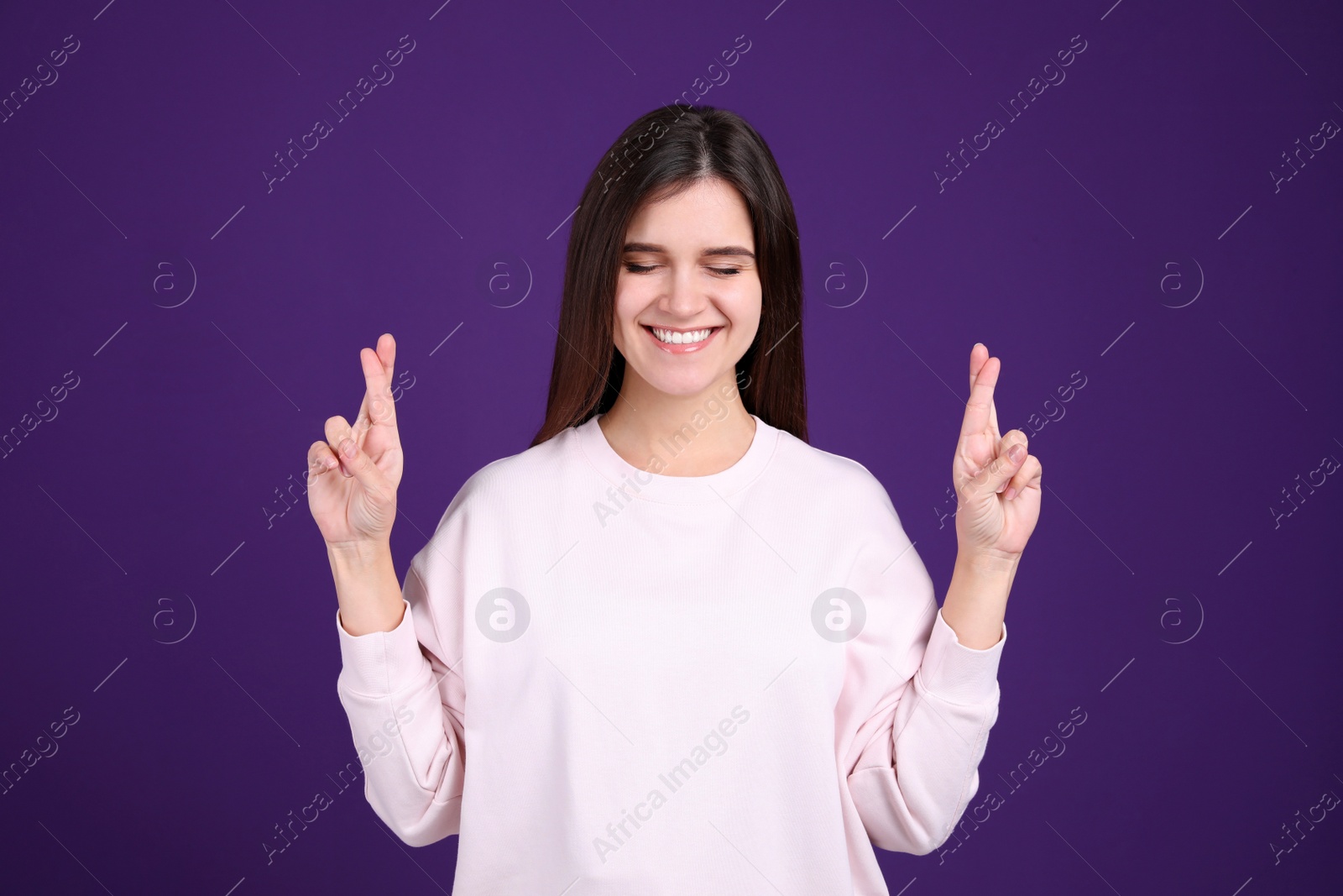 Photo of Happy young woman crossing fingers on purple background. Dealing with stress