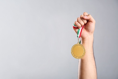 Man holding golden medal on grey background, closeup. Space for design