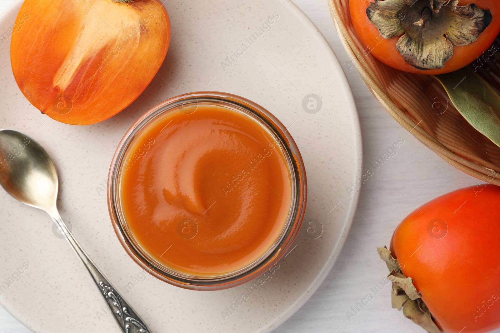 Photo of Delicious persimmon jam in glass jar served on white wooden table, flat lay