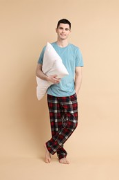 Happy man in pyjama holding pillow on beige background