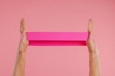 Photo of Woman with elastic resistance band on pink background, closeup of hands